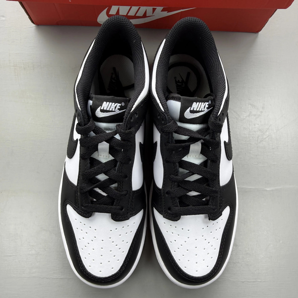 Nike Dunk Low white and black sneakers with retro panda design and logo.
