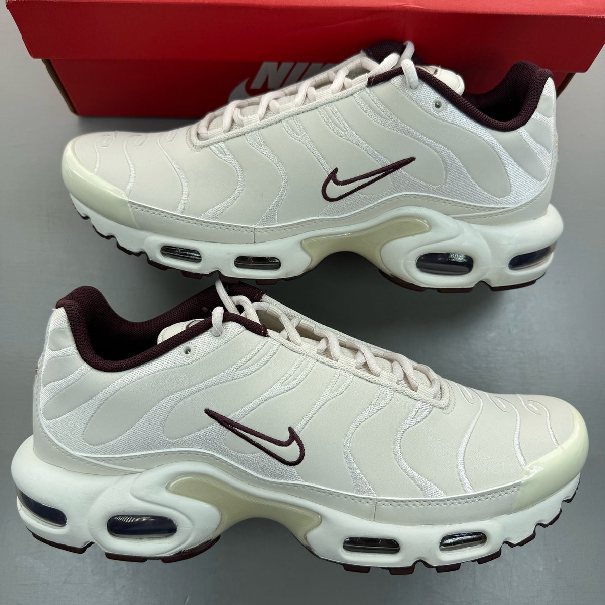 Nike Air Max Plus TN white trainers with burgundy accents and visible logo details.