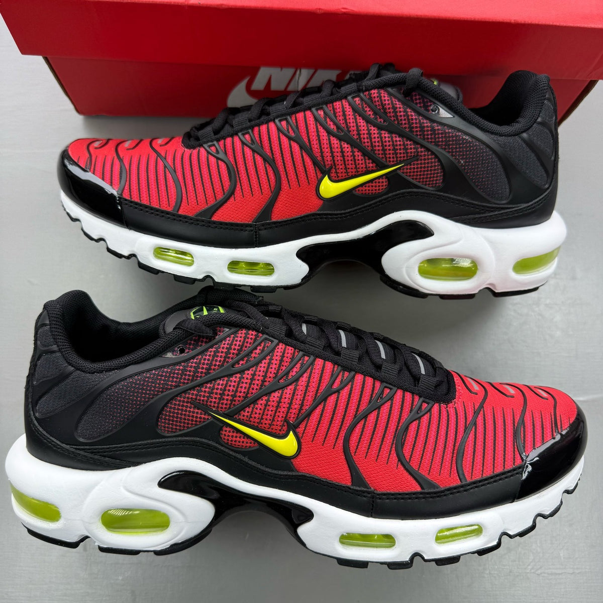 Nike Air Max Plus TN black trainers with light crimson and volt accents, logo on tongue.