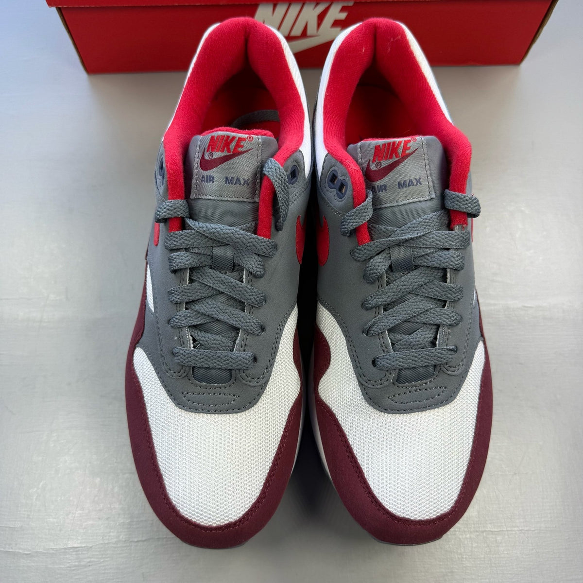 Nike Air Max 1 trainers grey red white with logo and mesh material details.