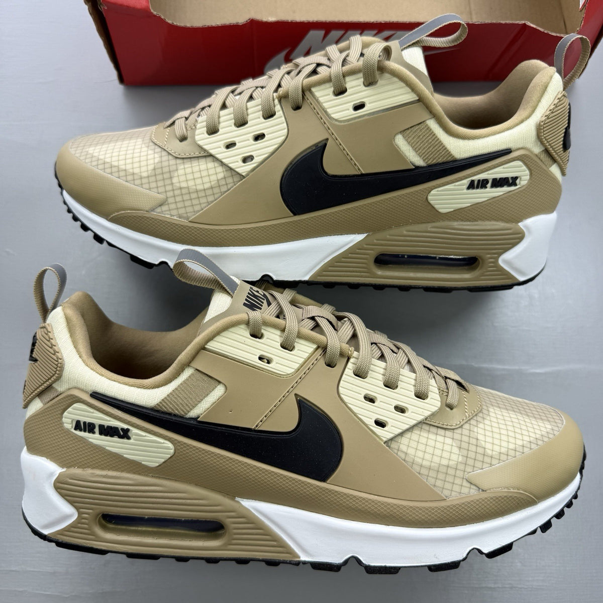 Nike Air Max 90 Drift beige trainers with black and white accents, featuring logo details.