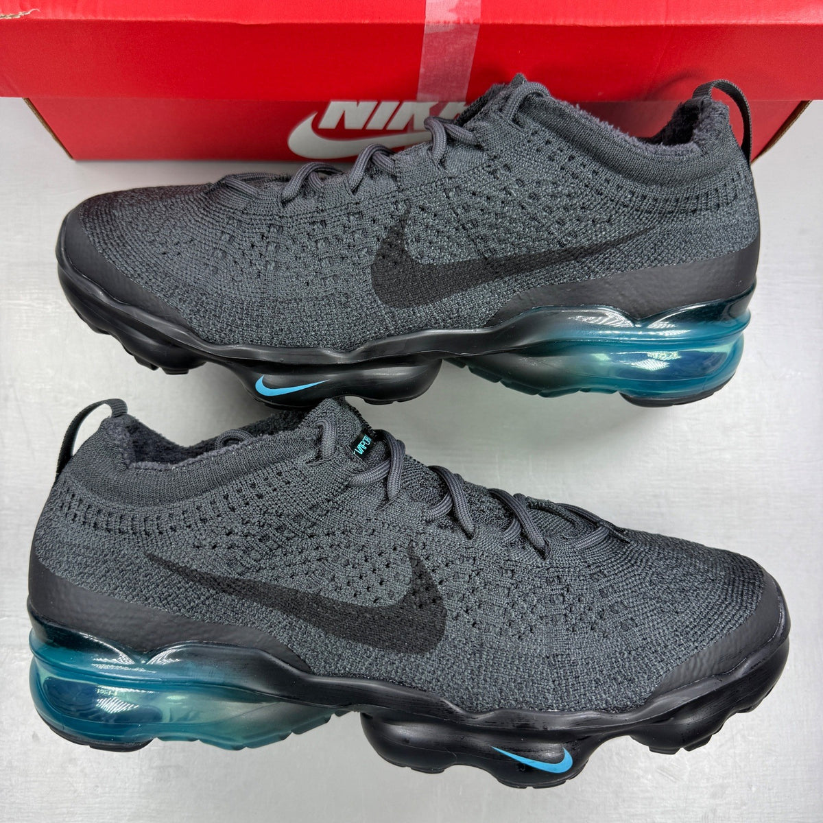 Nike athletic shoes grey Flyknit upper with Air VaporMax sole and logo detail.