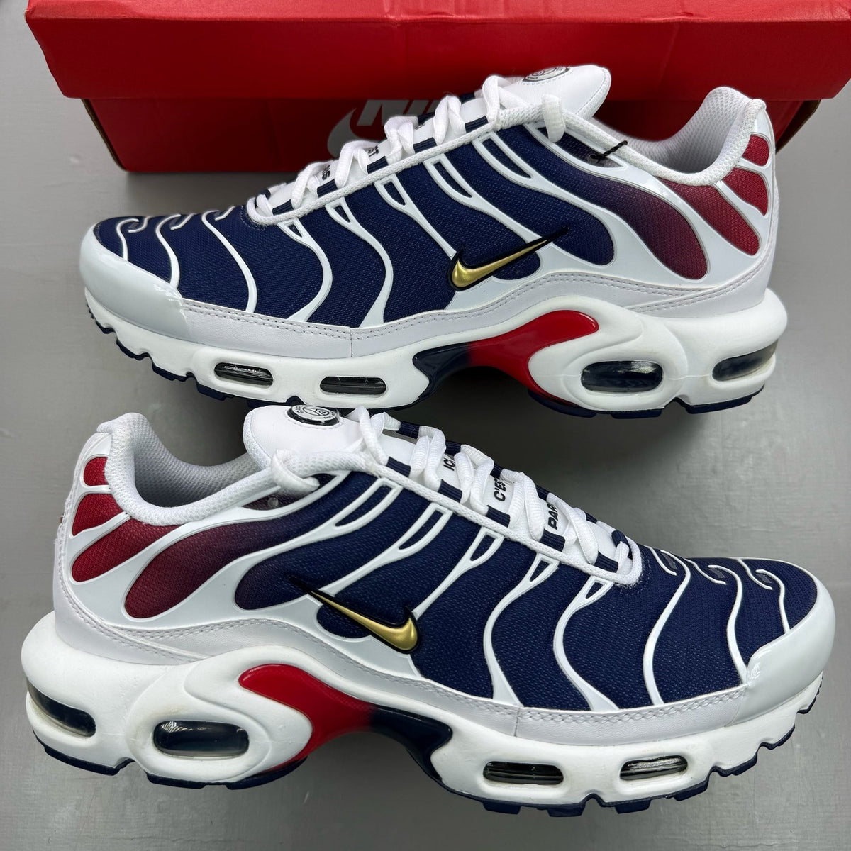 Nike Air Max Plus trainers white with navy and red accents, featuring logo details.