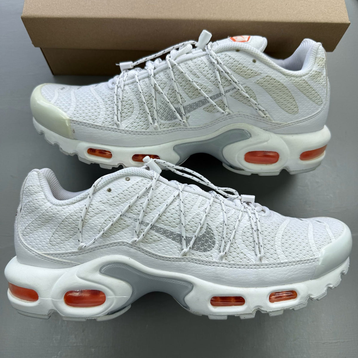 Nike footwear white trainers with orange accents and distinctive Air Max Plus TN design.