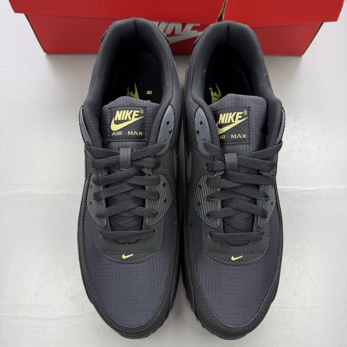 Nike Air Max 90 black trainers with buff gold and anthracite grey accents.