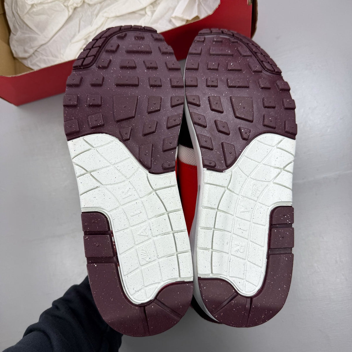 Nike Air Max 1 white trainers with burgundy accents and logo detailing.