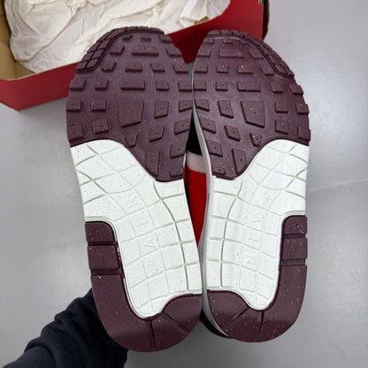 Nike Air Max 1 white trainers with burgundy accents and logo detailing.
