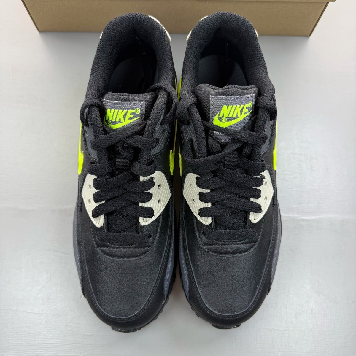Nike Air Max 90 black trainers with volt accents and signature logo detailing.