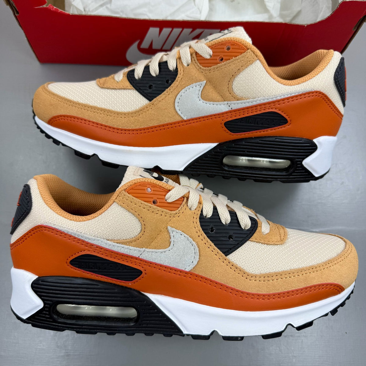 Nike Air Max 90 orange trainers with copper accents and signature swoosh logo.
