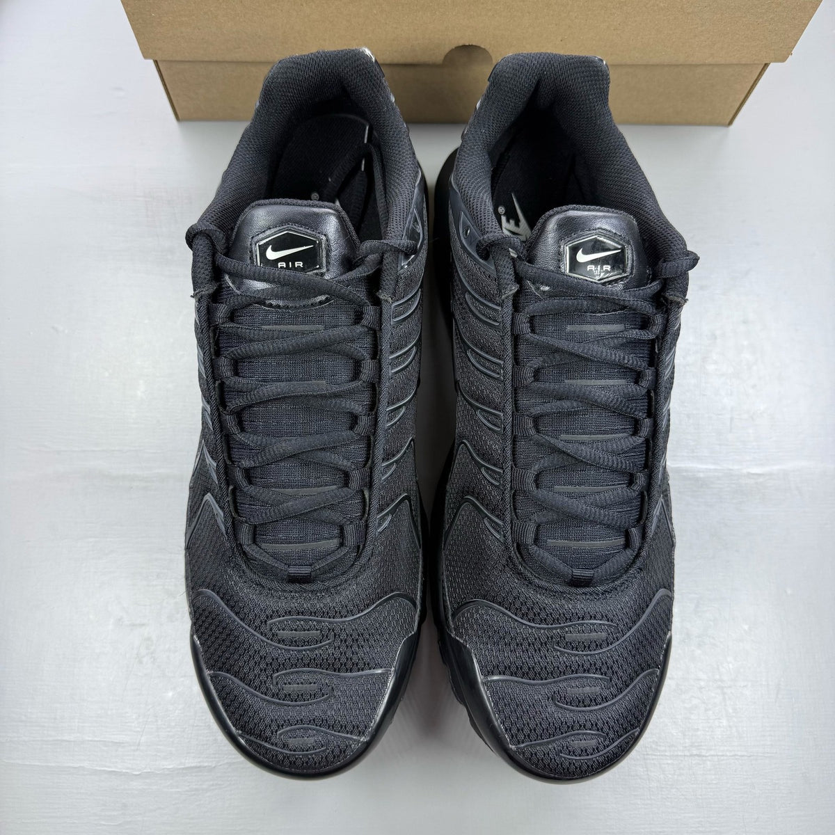 Nike Air Max Plus TN black trainers with distinctive wave pattern and logo detail.