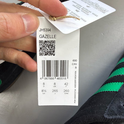 Adidas black Gazelle trainers with green accents and classic logo detailing.