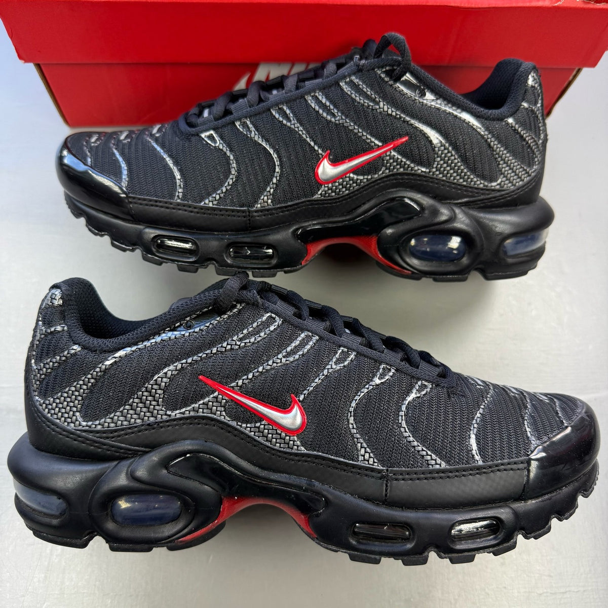 Nike Air Max Plus TN black trainers with university red accents and visible logo details.