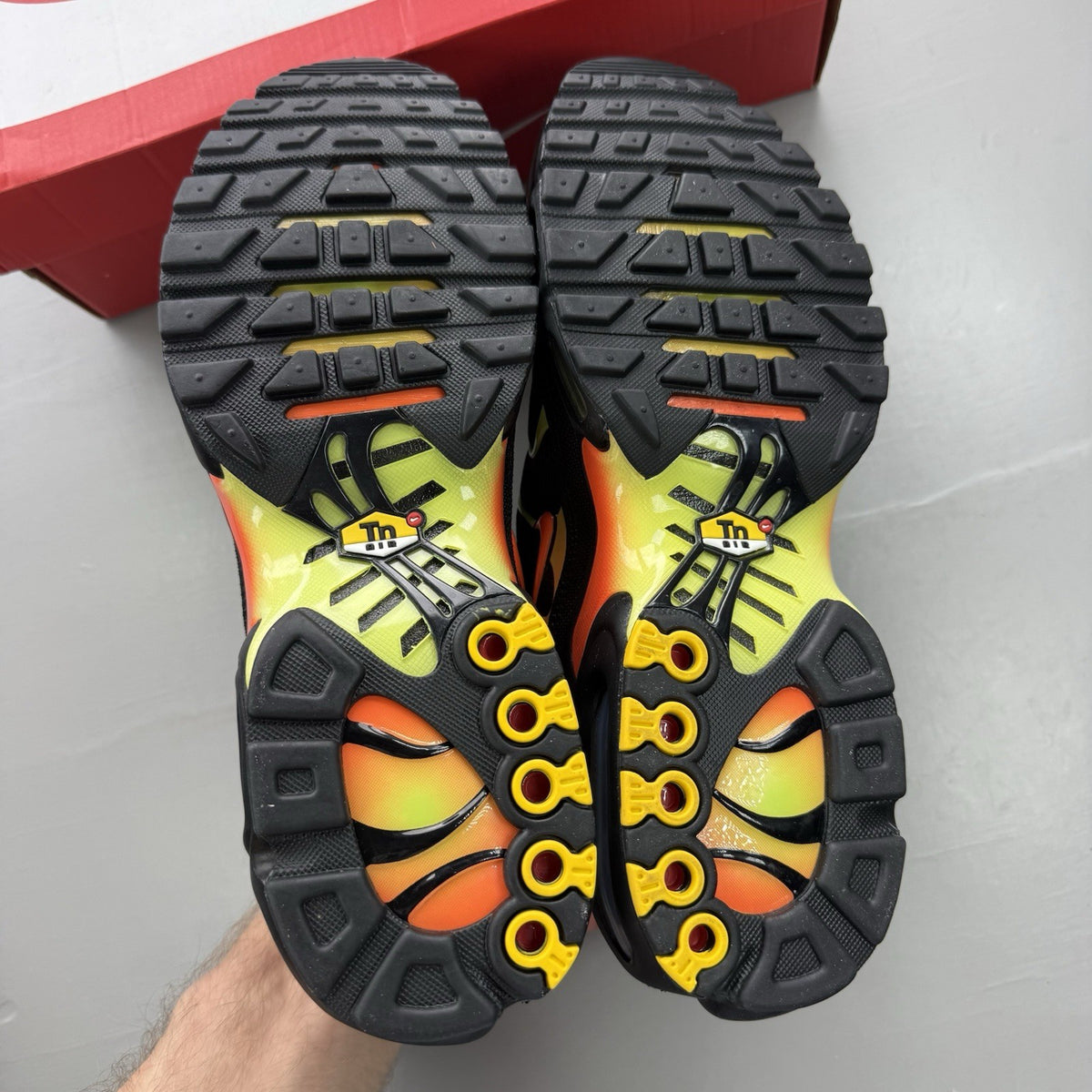 Nike Air Max Plus TN black trainers with vibrant orange and volt accents, mesh material.