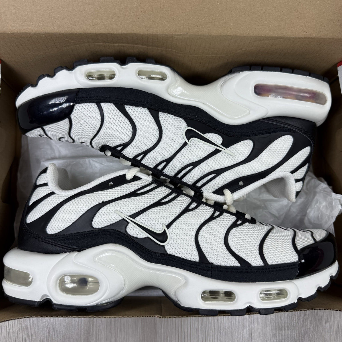 Nike Air Max Plus TN ESS trainers white with black accents and signature swoosh logo.