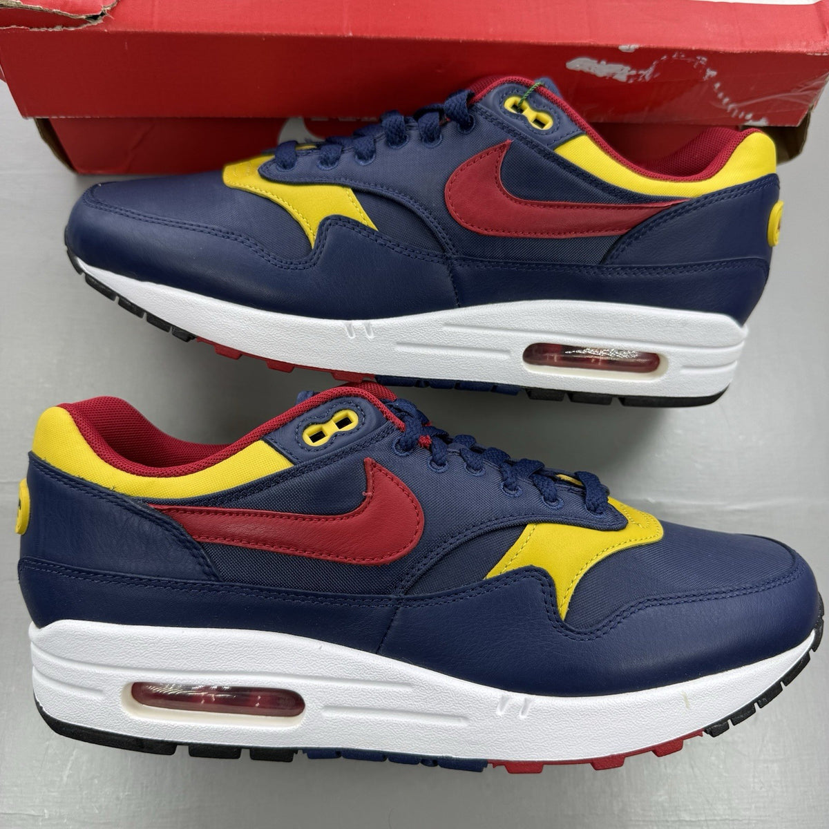 Nike Air Max 1 trainers blue with red and yellow accents, featuring iconic logo and design.