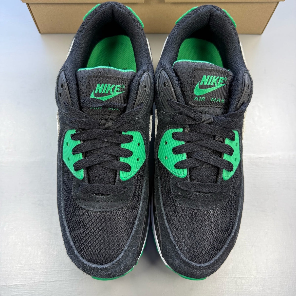 Nike Air Max 90 black trainers with green accents and white sole, featuring logo details.