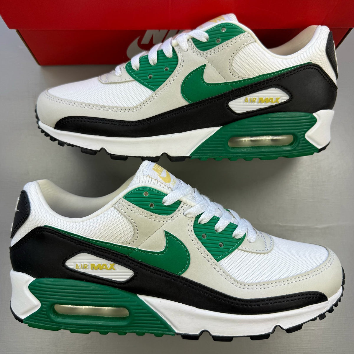 Nike Air Max 90 white trainers with green and black accents, featuring iconic logo details.