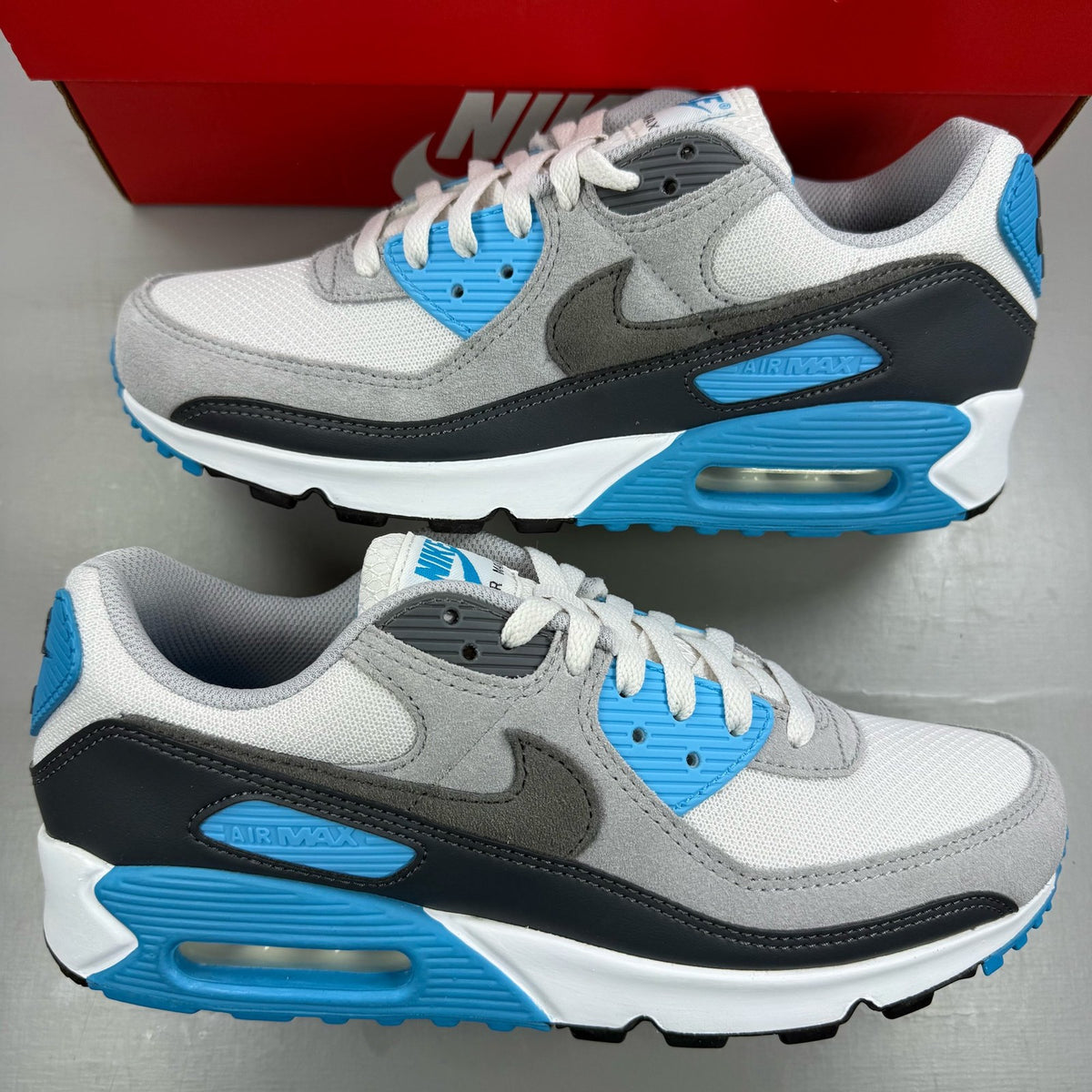 Nike Air Max 90 grey trainers with blue accents and signature swoosh logo.