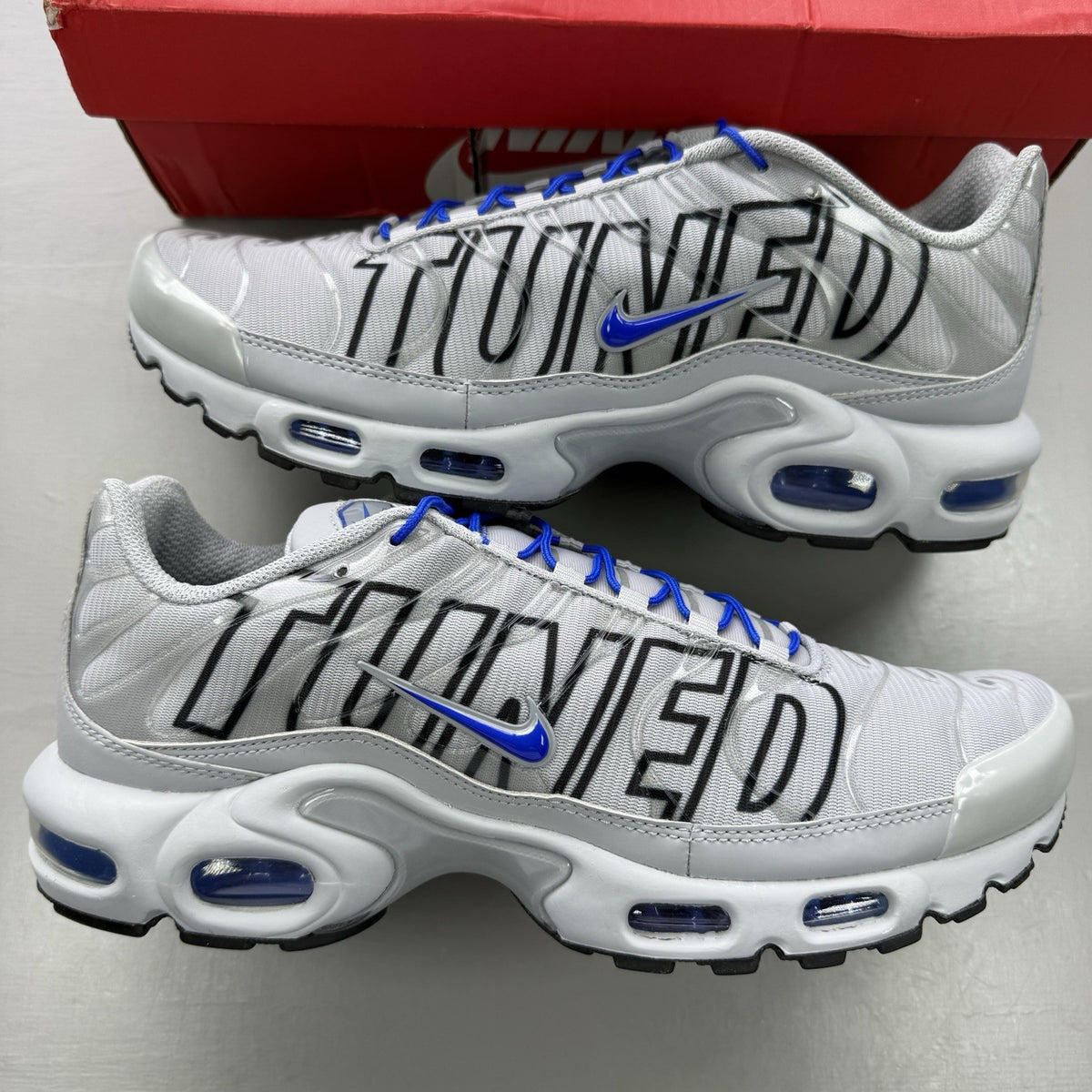 Nike Air Max Plus TN trainers grey with blue accents and signature swoosh logo.