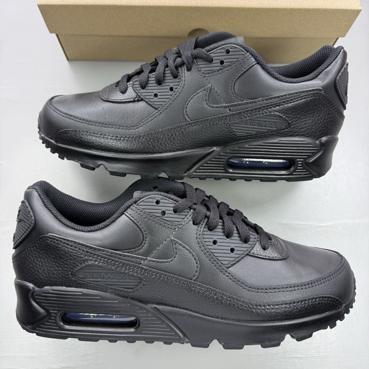 Nike Air Max 90 trainers black leather with signature swoosh logo and textured detailing.