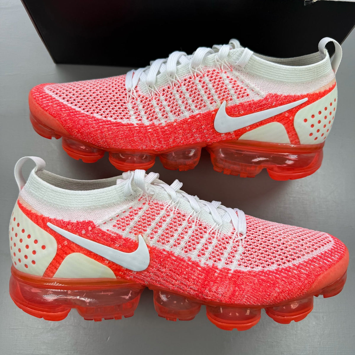 Nike Air VaporMax 2 Flyknit white trainers with hot punch red accents and breathable material.