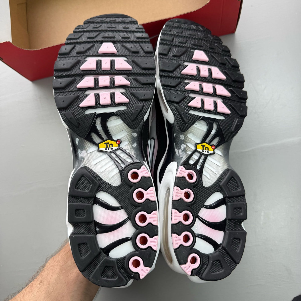 Nike Air Max Plus TN black trainers with pink accents and signature swoosh logo.