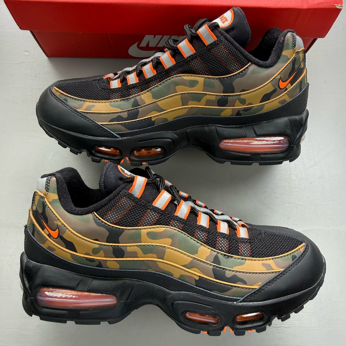Nike Air Max 95 black trainers with orange camo accents and logo details.