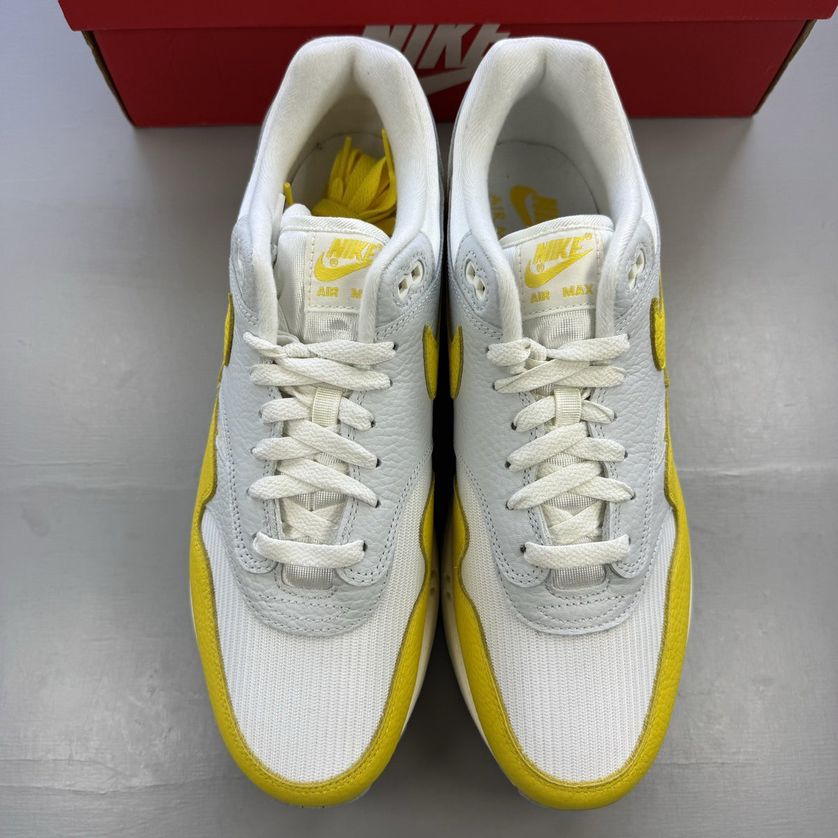 Nike Air Max 1 white trainers with yellow accents and grey detailing.