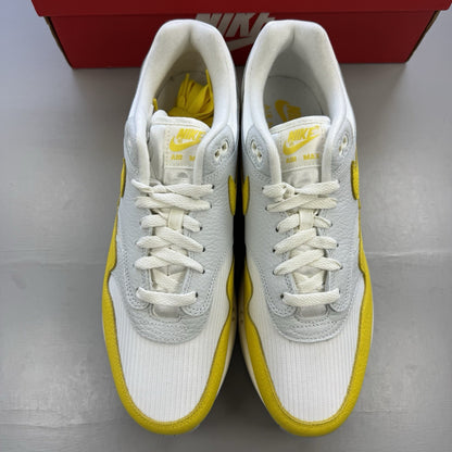 Nike Air Max 1 white trainers with yellow accents and grey detailing.