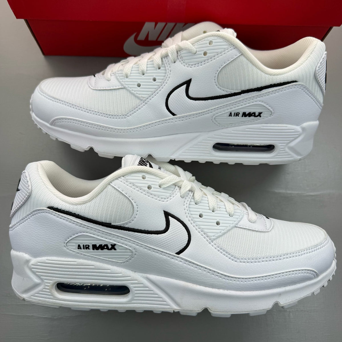 Nike Air Max 90 white trainers with black outlined swoosh logo and mesh material.