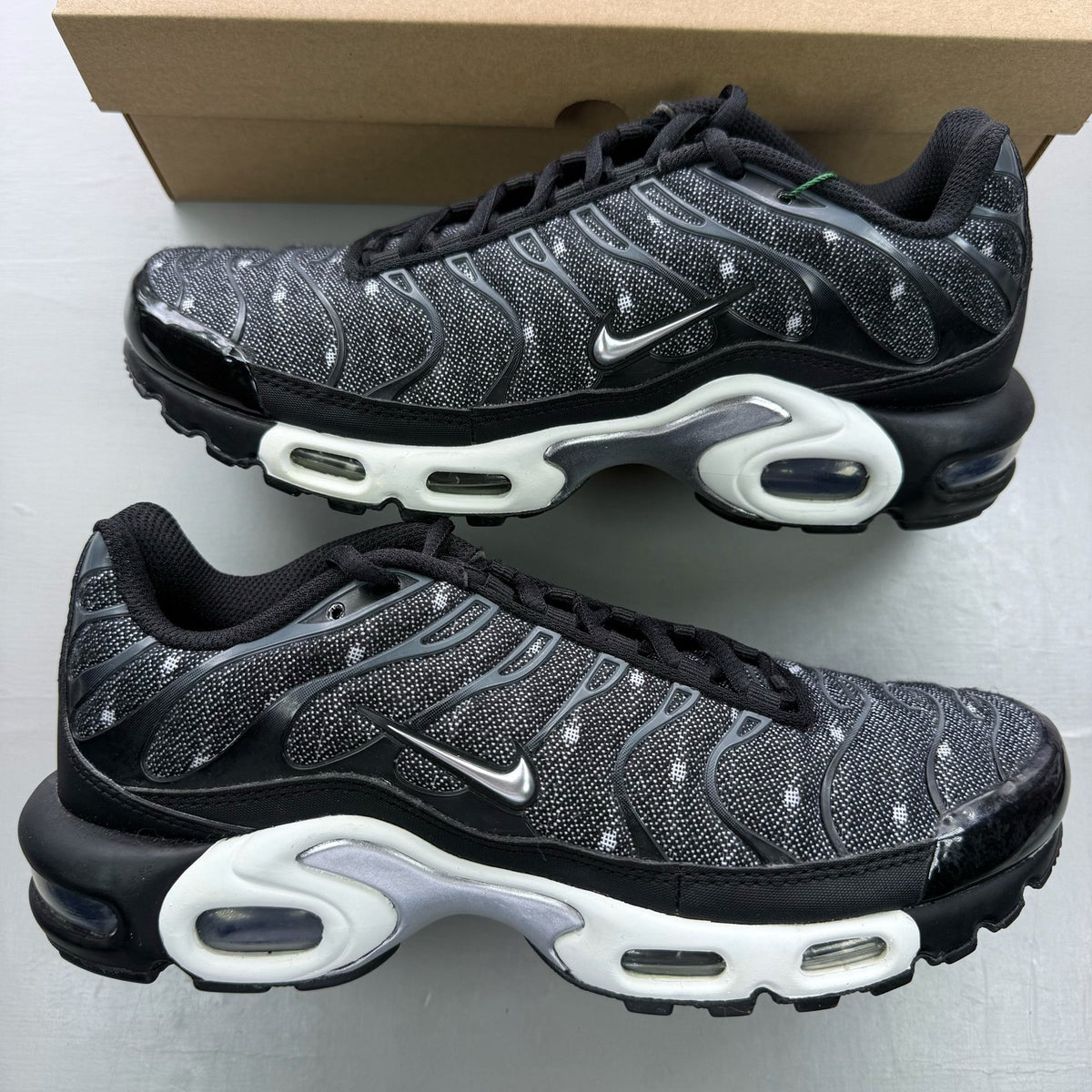 Nike Air Max Plus TN black trainers with chrome accents and distinctive wave pattern.