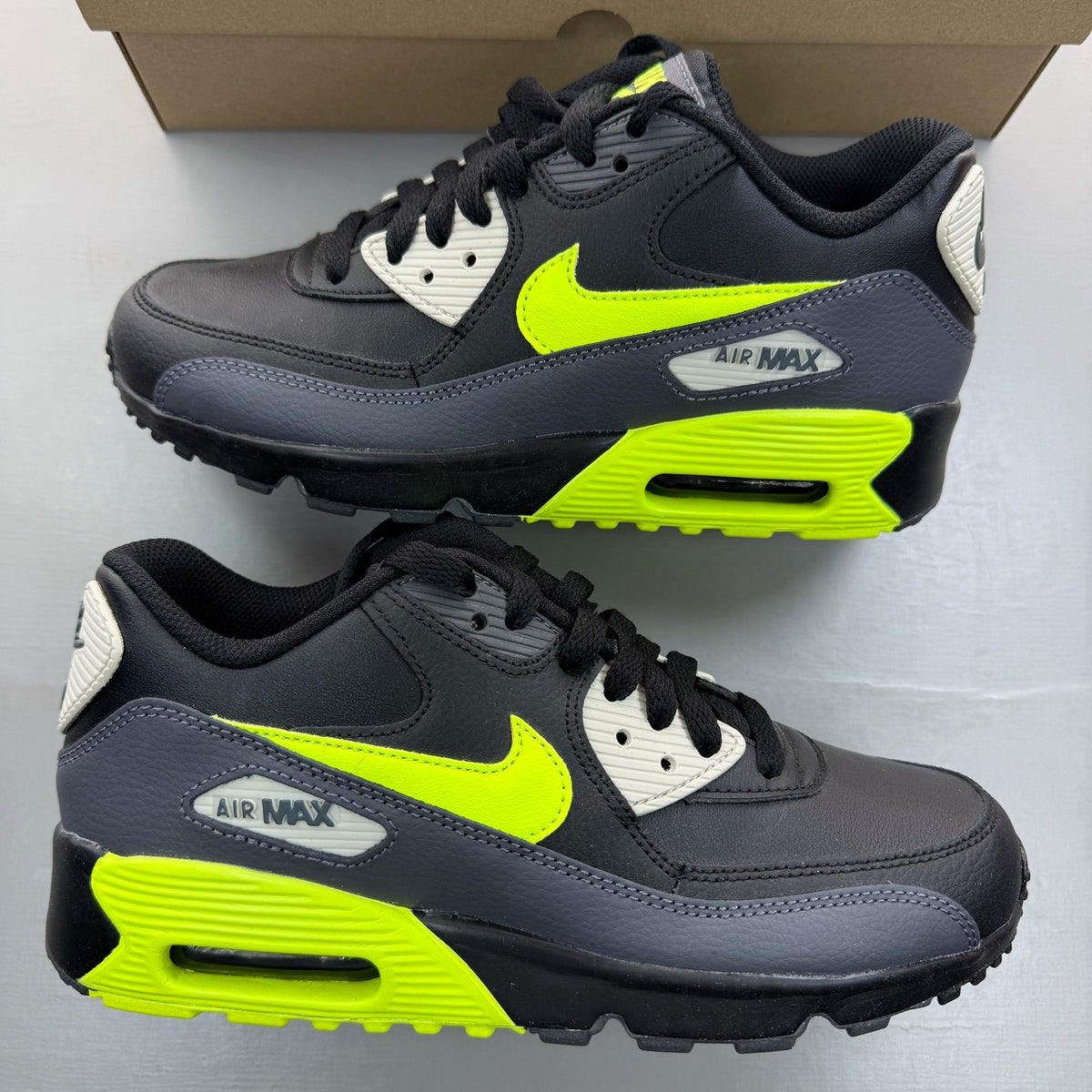 Nike Air Max 90 black trainers with volt accents and signature logo detailing.