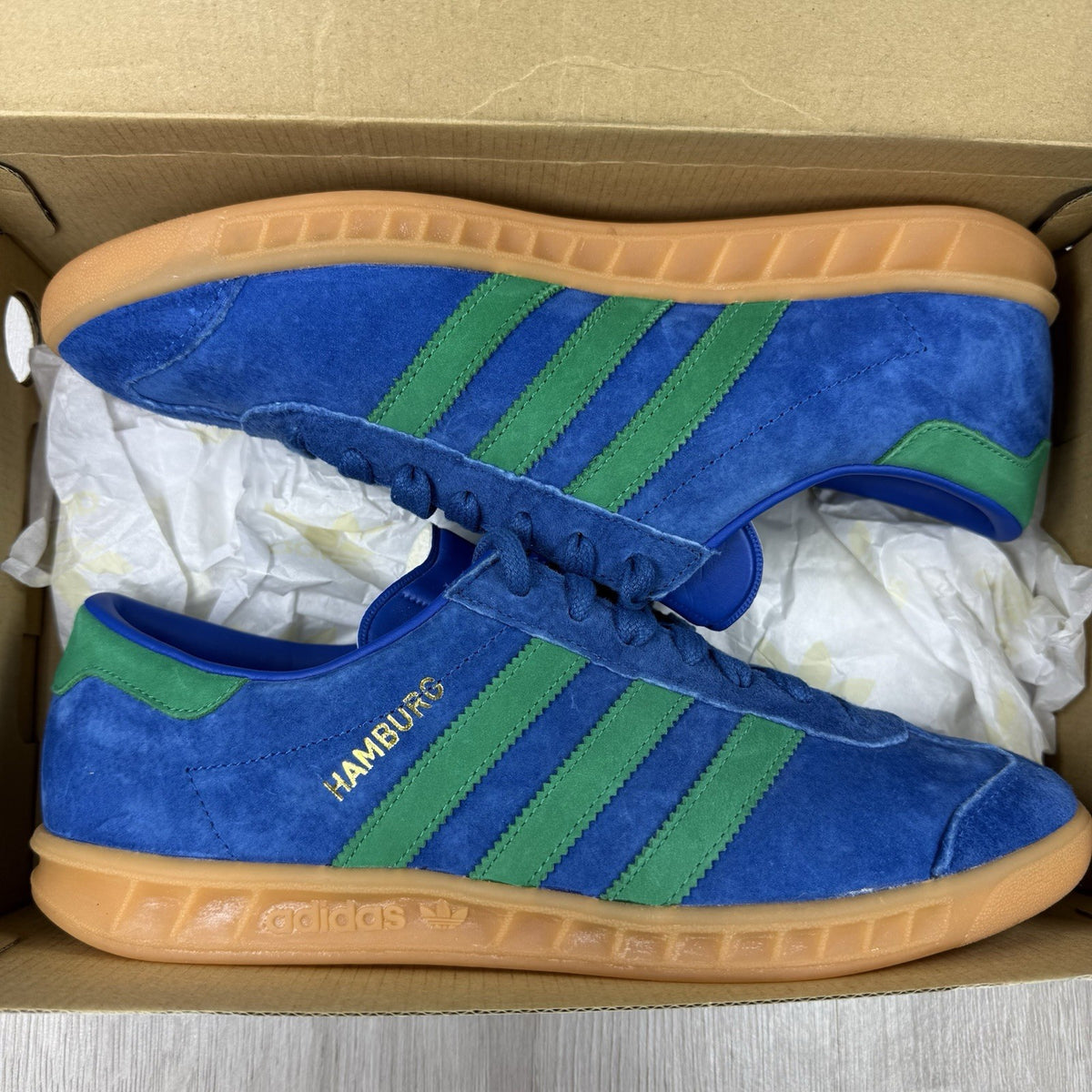 Adidas blue trainers with gum sole and iconic three-stripe logo design.