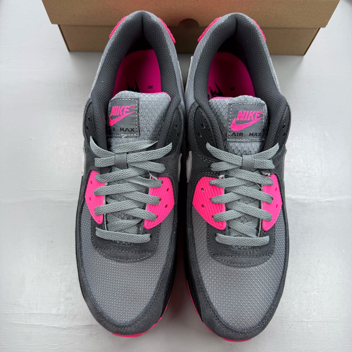 Nike Air Max 90 grey trainers with hyper pink accents and black detailing.