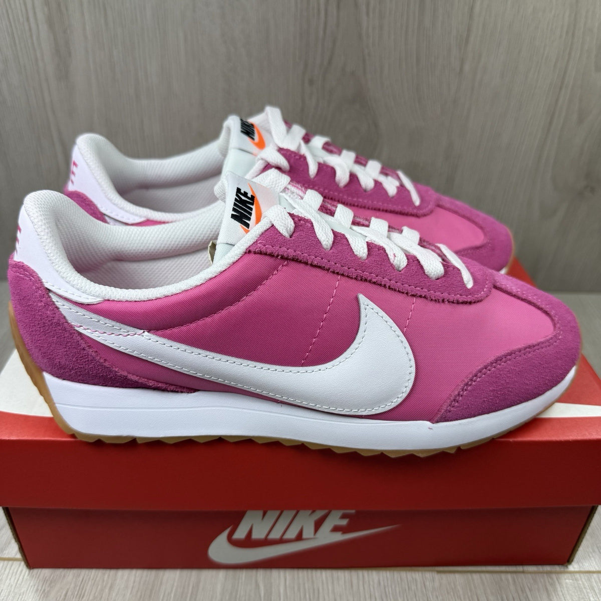 Nike white trainers with pink accents and gum sole, featuring iconic swoosh logo.
