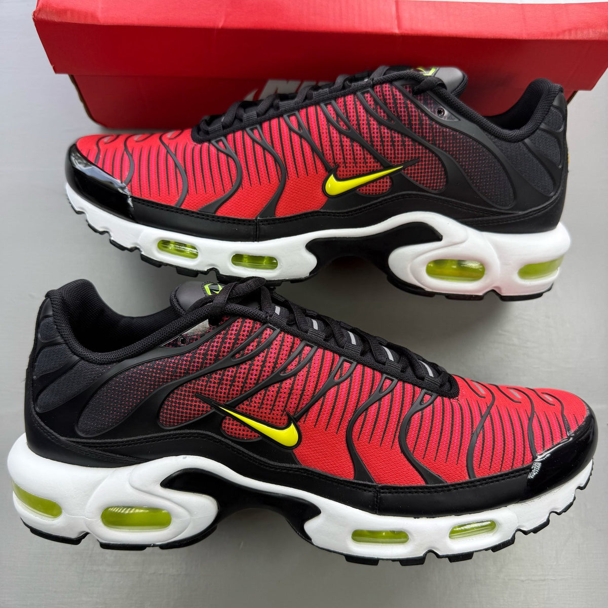 Nike Air Max Plus TN red trainers with black accents and vibrant volt detailing.
