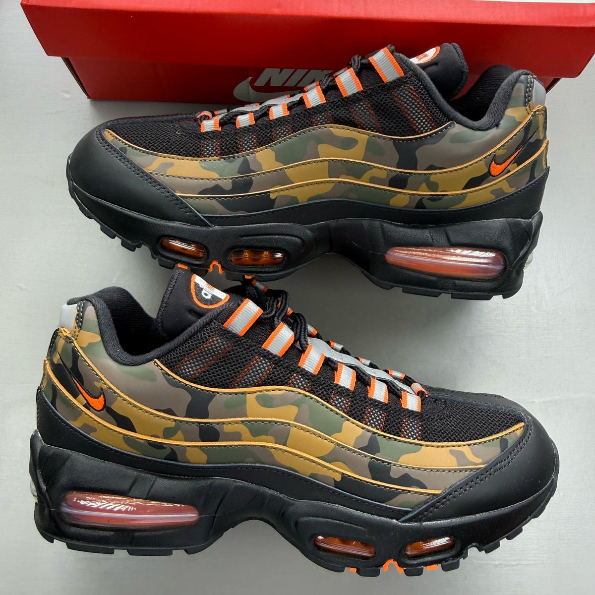Nike Air Max 95 black trainers with orange camo accents and signature swoosh logo.