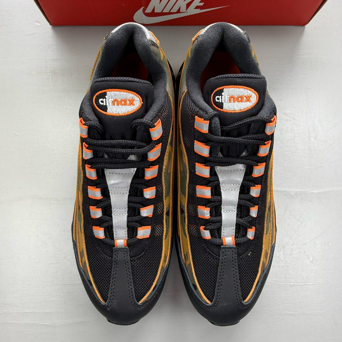 Nike Air Max 95 black trainers with orange camo accents and signature swoosh logo.