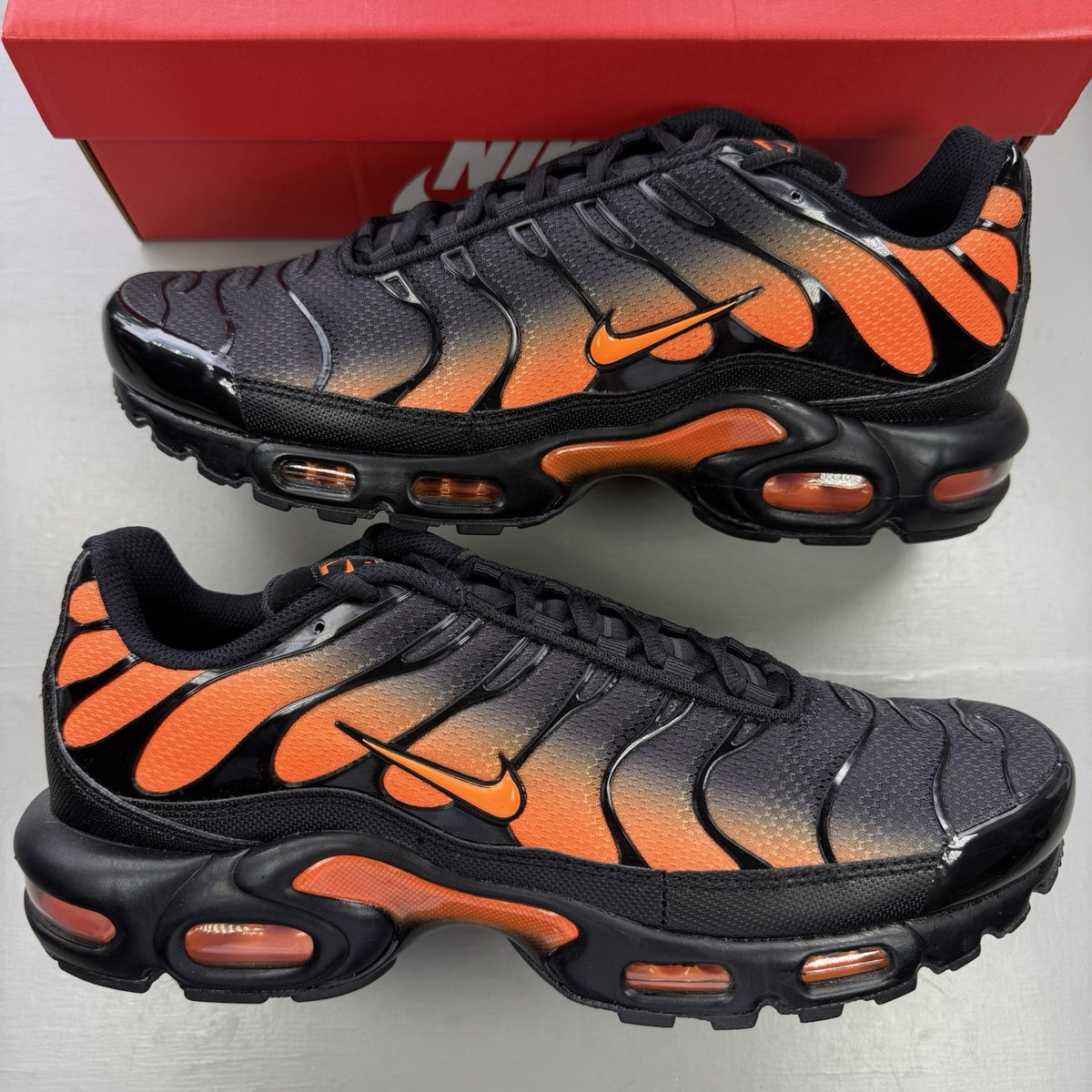 Nike Air Max Plus TN black trainers with total orange accents and signature logo.