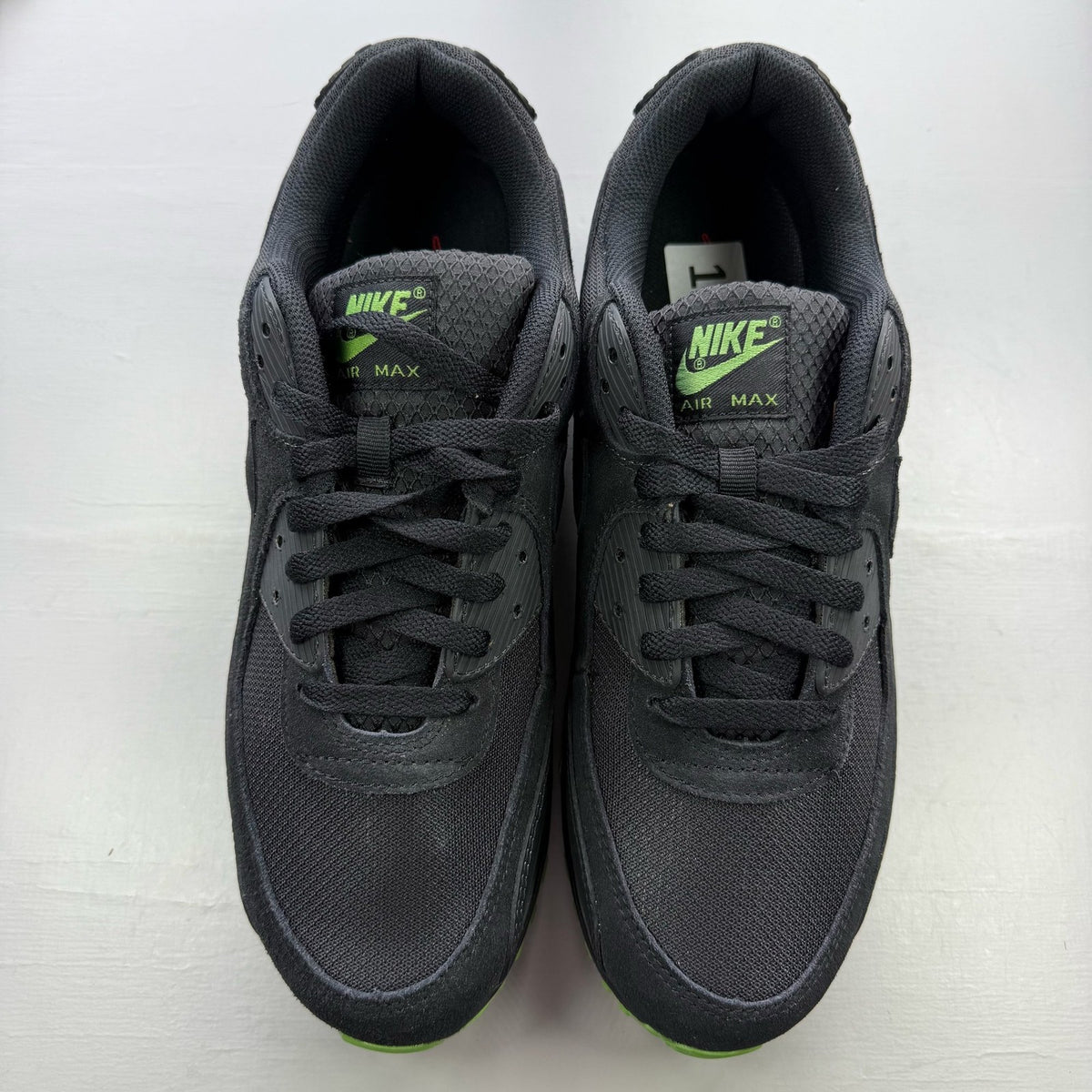 Nike Air Max 90 black trainers with green accents and logo detail on the tongue.