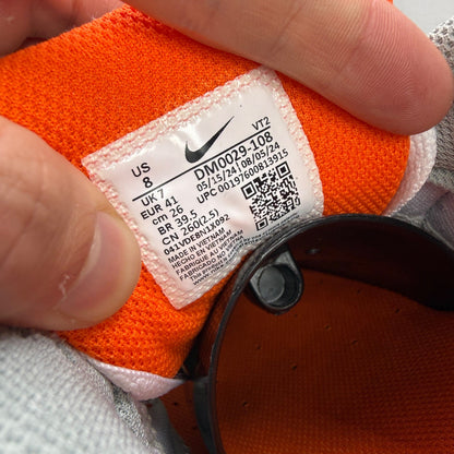 Nike Air Max 90 white trainers with safety orange accents and grey detailing.