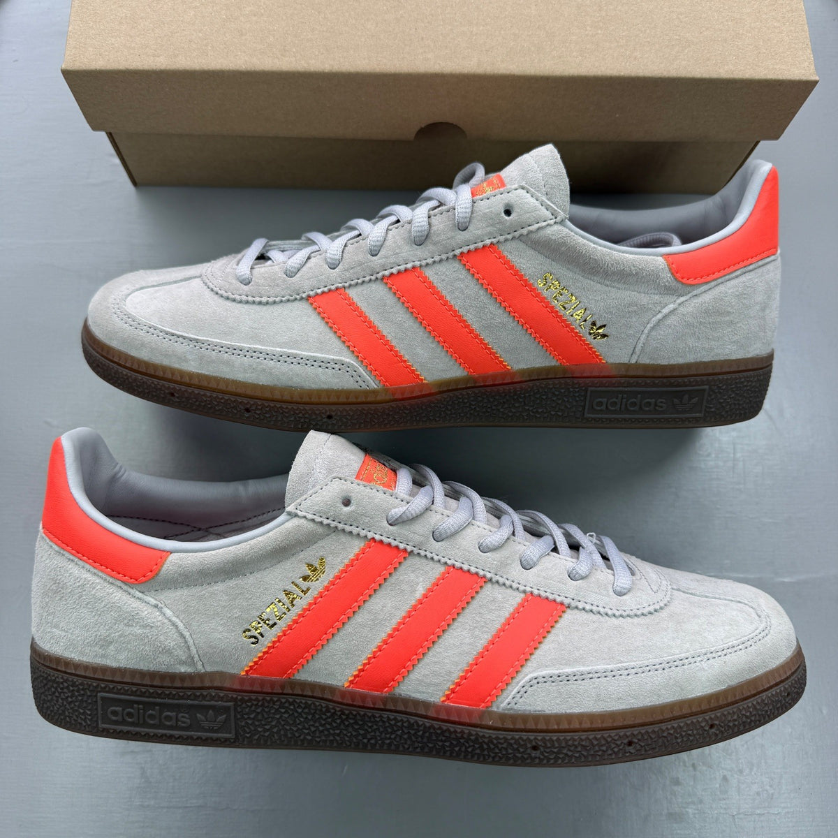 Adidas grey trainers with coral accents and gum sole, featuring classic logo.