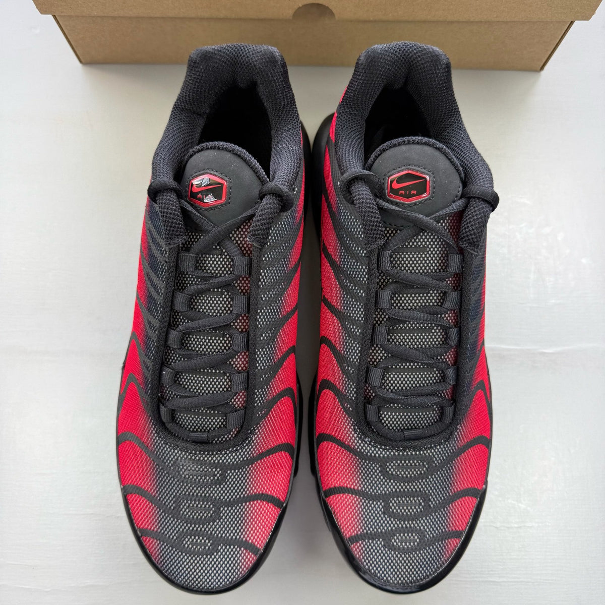 Nike black Air Max Plus TN trainers with reflective accents and red detailing.