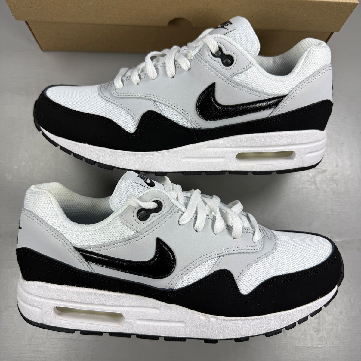 Nike Air Max 1 white trainers with black and grey accents, featuring logo details.