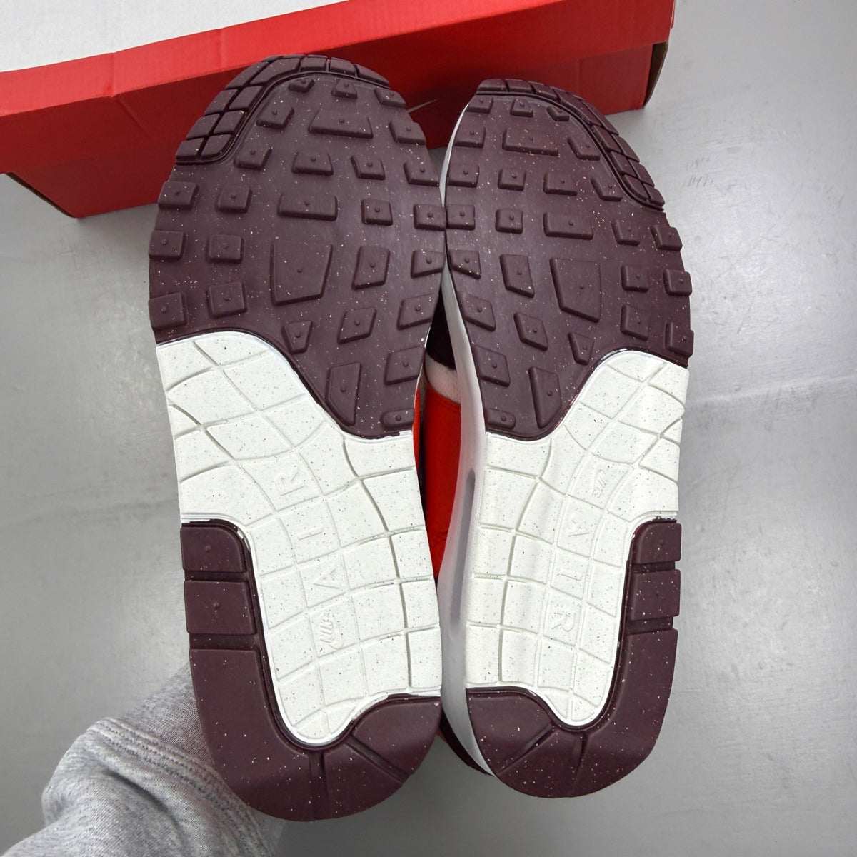 Nike Air Max 1 white trainers with burgundy accents and logo detail.