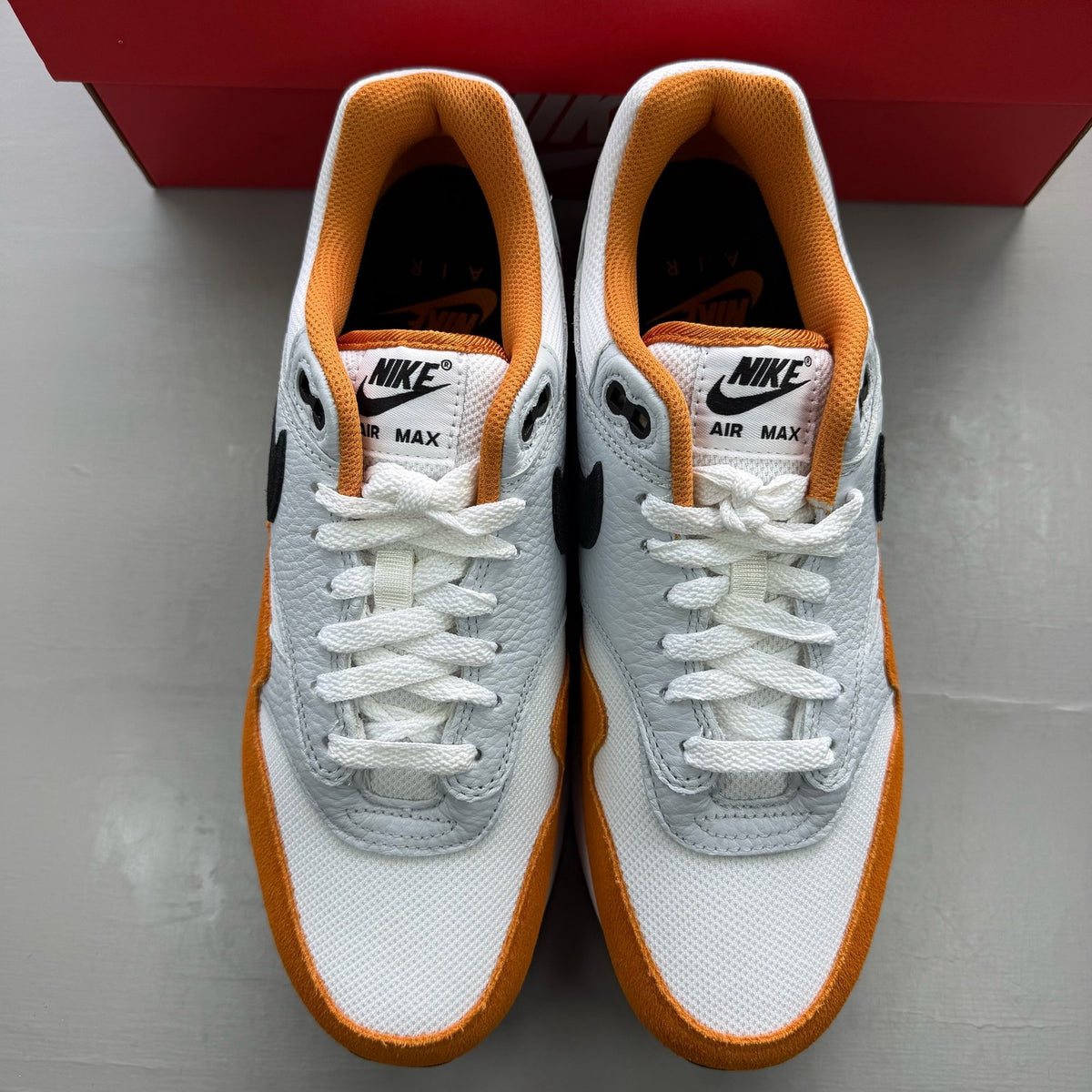 Nike Air Max 1 white trainers with Monarch orange and black accents, featuring logo details.