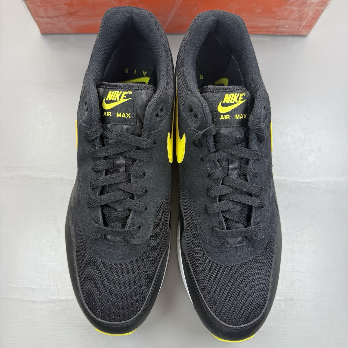 Nike Air Max 1 Essential black trainers with yellow accents and logo detail.