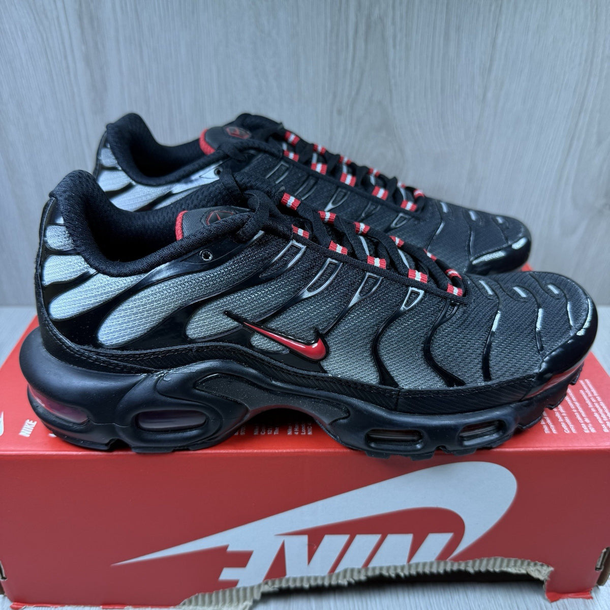 Nike TN Air Max Plus trainers black with red gradient and signature logo design.