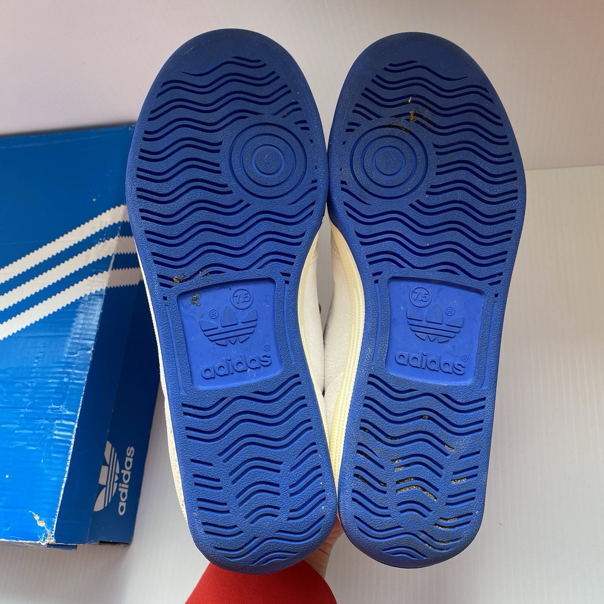 Adidas white trainers with blue and beige accents, featuring classic logo detail.