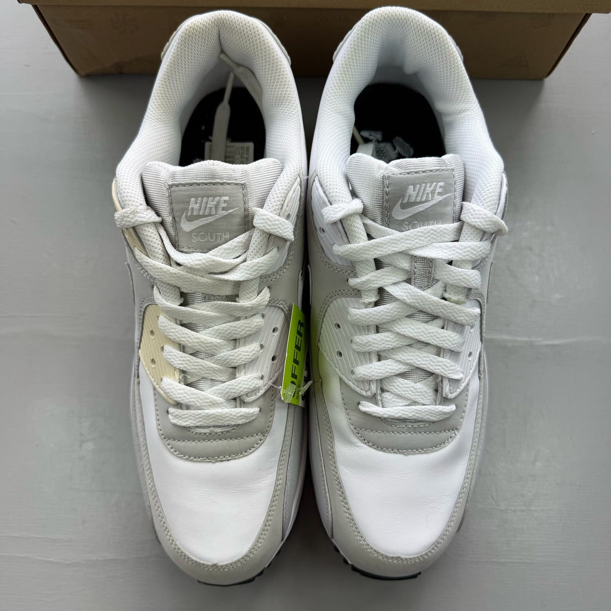 Nike Air Max 90 white trainers with grey accents and logo detailing.